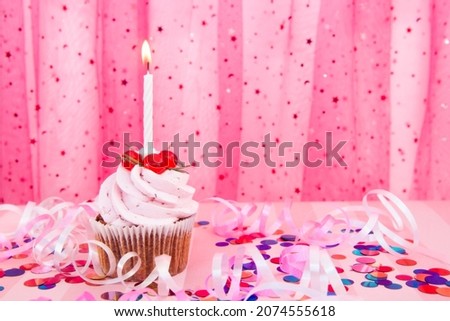 Pink cupcake and white one candle on colorful background with decorations and copy space , happy birthday and anniversary card
