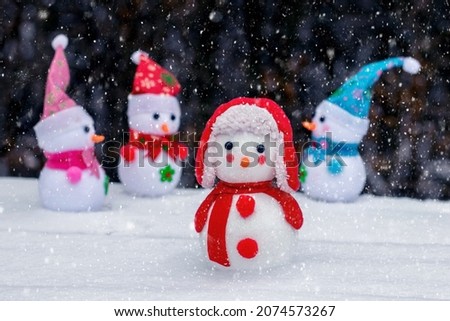 Cheerful snowmen in the woods in the snow on a dark background during a snowfall