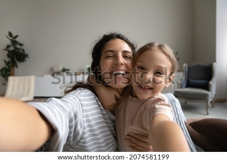 Head shot portrait of smiling mother and daughter taking selfie, hugging and looking at camera, laughing mom with adorable girl child having fun with webcam together, bloggers recording video