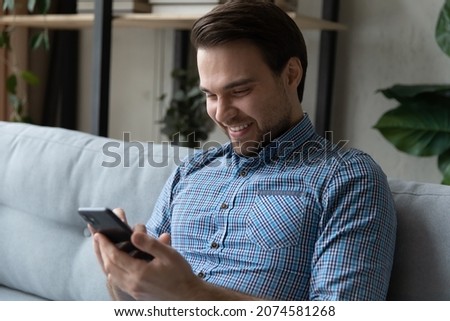 Sincere happy young man using cellphone, enjoying playing mobile games, web surfing information, having fun watching photo or video content online in social network, shopping in internet store. Royalty-Free Stock Photo #2074581268