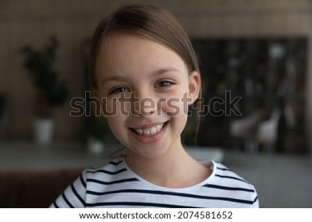 Head shot portrait of smiling 8s Caucasian girl child looking at camera, adorable happy kid having fun with webcam, making video call online, engaged in conference, blogger shooting recording