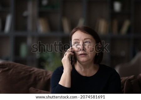 Head shot close up of serious mature woman talking on phone at home sitting on couch, senior female holding mobile device smartphone, chatting with relatives or friends, making or answering call Royalty-Free Stock Photo #2074581691