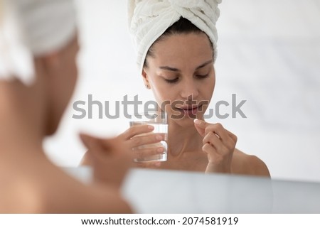 Close up head shot beautiful young hispanic mixed race woman taking pill drinking glass of fresh water after morning shower, daily omega vitamins, dietary supplements for nails hair skincare. Royalty-Free Stock Photo #2074581919