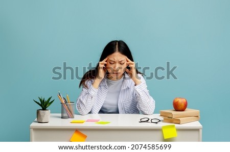 Tired asian lady feeling headache or stress, massaging her temples, trying to learn and study, doing homework and thinking, sitting at desk over blue background Royalty-Free Stock Photo #2074585699