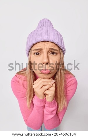 Photo of sad frustrated young woman with pity expression purses lips has pleading expression wears knitted hat and pink jumper isolated over white background asks for apology. Please forgive me