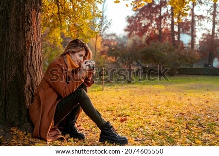 Pretty young woman taking pictures with analog camera in the park in autumn 