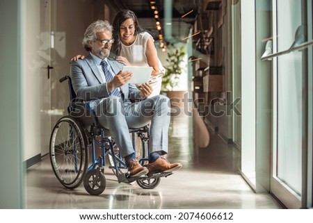 Disabled Male Manager Sitting With His Colleagues At Workplace. Portrait of smiling disabled business executive in wheelchair at meeting. Happy male entrepreneur in a wheelchair