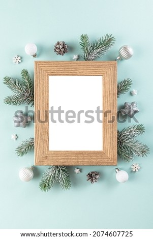 Christmas or Happy New Year blank photo frame with fir tree branches, holiday decorations on blue background. Flat lay. Mock up. Top view. Vertical orientation