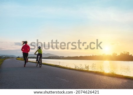 Happy mother and son go in sports outdoors. Boy rides bike in helmets, mom runs on sunny day. Fresh air. Health care, authenticity, sense of balance and calmness