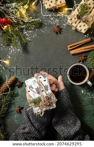 Winter concept. Flatlay composition with female hands hold Christmas present and of coffee on a dark stone background. Copy space.