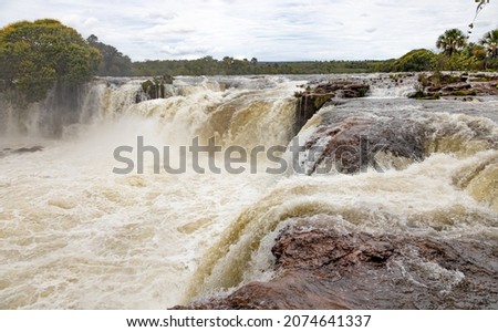 Waterfall with large volume of water and stones in brown tones and buriti feet in the background with native vegetation in Jalapão State Park.