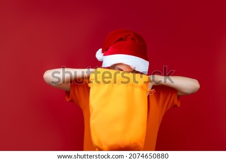 a boy with a Santa Claus Christmas hat opens yellow gift bags and looks in there