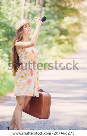 happy young girl with vintage camera and valise walking outdoors in the park