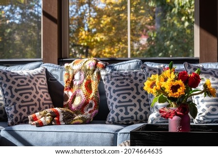 Cozy patio corner in a screened porch with flower bouquet in a vase, autumn leaves and woods in the background.
