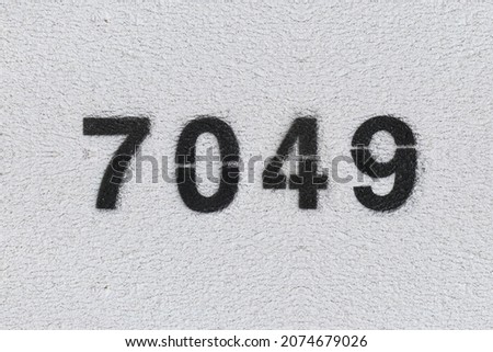 Black Number 7049 on the white wall. Spray paint. Number seven thousand forty nine.