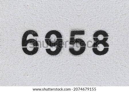 Black Number 6958 on the white wall. Spray paint. Number six thousand nine hundred fifty eight.
