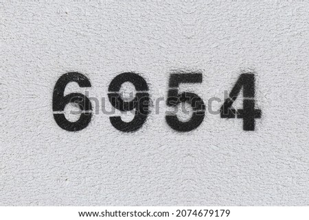 Black Number 6954 on the white wall. Spray paint. Number six thousand nine hundred fifty four.