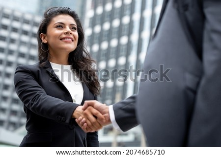 Young smiling Hispanic businesswoman making handshake with partner in the city for greeting, dealing, merger and acquisition concepts Royalty-Free Stock Photo #2074685710