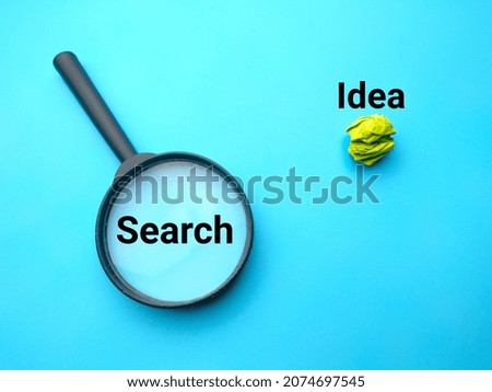 Magnifying glass and colored crumpled paper with text search idea on a blue background.