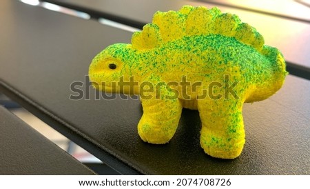 Small greenish yellow dinosaur toy on a solid black metal table