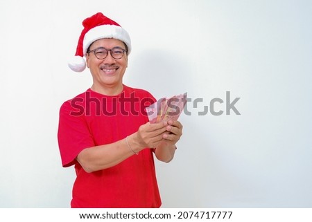 Man wearing red and Santa's hat counting money from Christmas bonus