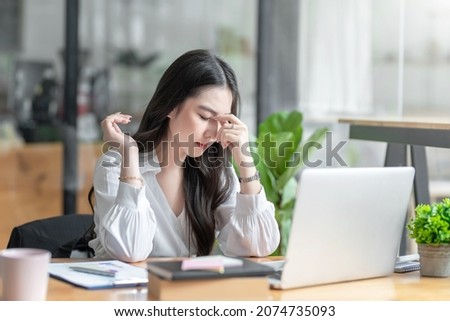 Young Asian woman feeling migraine head strain. Tired, Overworked businesswoman financier while working on laptop computer in office. Royalty-Free Stock Photo #2074735093