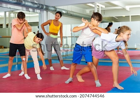 Focused kids in pair exercising self-defense movements during group class with female coach