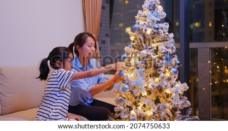 Happy mother and daughter decorate christmas tree together at home