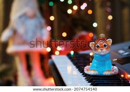 2022. Year of the tiger. Happy Chinese New Year. Christmas tree toy on the piano keys. Colored lights of an electric garland and a silhouette of a gnome in blur. Musical instrument. Selective focus.