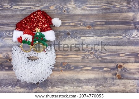 The head of Santa Claus in gold holiday glasses and with a beard made of artificial snow on a dark wooden background. Winter Christmas landscape with copy space.