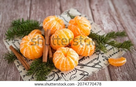 Orange mandarins or tangerines and cinnamon sticks on branches Christmas tree on brown wooden background.
