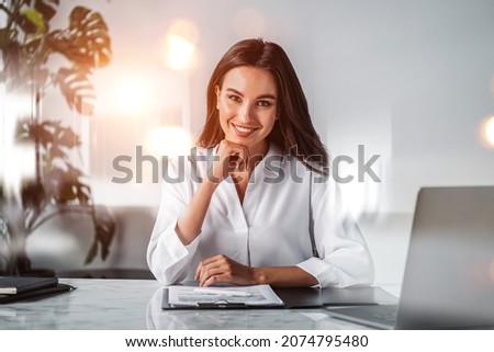 Office woman happy look in white office room, bokeh lights, laptop and clipboard with papers on the table. Desk with notebook and technology. Concept of business secretary Royalty-Free Stock Photo #2074795480