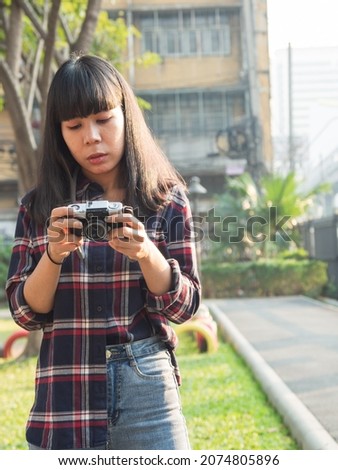 Portrait yong woman Asian girl 20-25 years long black hair red shirt dark red Taking picture with toy camera in park With sun shining down In evening Happily on a bright day Relax with her vacation