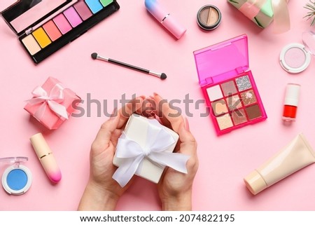 Woman with Christmas gifts and decorative cosmetics on pink background