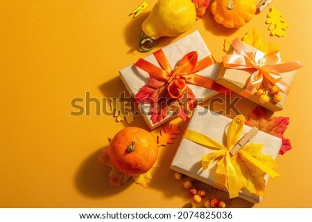 Gift concept in autumn colors. Wrapped boxes, festive fall decor, pumpkin, leaves, and berries. A trendy hard light, dark shadow, orange background, top view Royalty-Free Stock Photo #2074825036