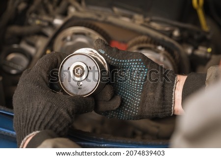 Auto mechanic inspects the timing belt tensioner roller of a passenger car, close-up Royalty-Free Stock Photo #2074839403