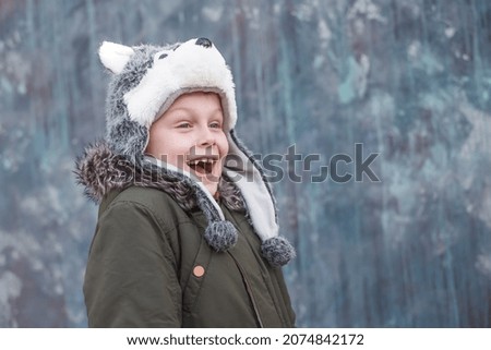 Portrait of a surprised child in a wolf hat and smiles sweetly on gray background, outdoor. space for text. High quality photo