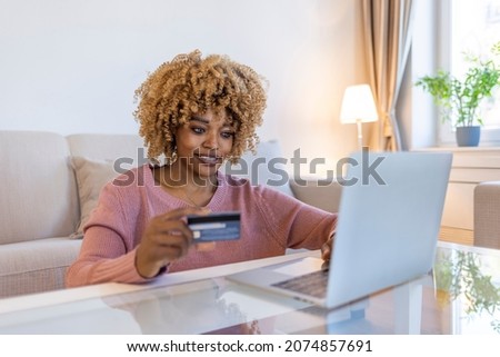 Smiling young woman holding a credit card and typing on a laptop. Cropped shot of an attractive young woman sitting on her sofa at home and using her laptop for online shopping