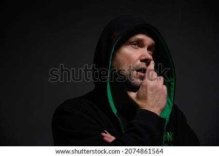 Portrait of an adult man in a hood looking to the side with an open mouth on a gray background
