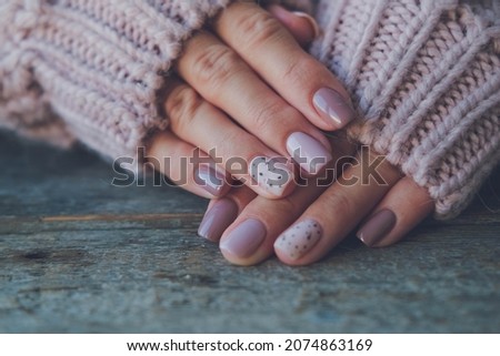 Women is hands with a beautiful manicure, in a knitted sweater on a wooden background in. Autumn trend, polish the beige and quail egg pattern on the nails with gel polish, shellac. Copy space.