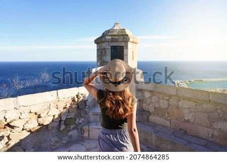 Tourism in Alicante, Spain. Back view of traveler girl walking towards watchtower on Santa Barbara castle in Alicante city, Spain. Young female tourist visiting southern Europe. Royalty-Free Stock Photo #2074864285