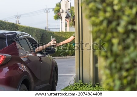 Hand Man in car receiving coffee in drive thru fast food restaurant. Staff serving takeaway order for driver in delivery window. Drive through and takeaway for buy fast food for protect covid19. Royalty-Free Stock Photo #2074864408