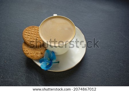 A cup of coffee and a cookie and a blue flower. Blue orchid, coffee, biscuit, zarne background. Picture with space for text.