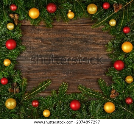 Close up border frame of fresh green spruce Christmas tree branches with cones and colorful balls and baubles decoration, over dark brown wooden planks background with copy space