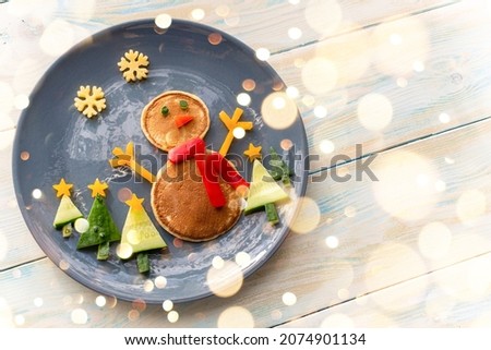 Christmas pancake healthy shaped like a snowman with fresh vegetables blue plate on wooden white table decorated festively. Christmas fun food for kids, funny breakfast brunch idea xmas
