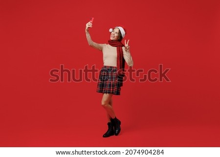 Full body young woman 20s wear Santa Claus Christmas hat doing selfie shot photo on mobile cell phone show victore sign isolated on plain red background studio. Happy New Year 2022 celebration concept