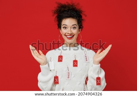 Young shocked amazed impressed fun cool happy female costumer woman 20s wearing white knitted sweater with tags sale in store showroom spreading hands isolated on plain red background studio portrait