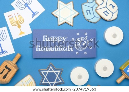 Different symbols of Hanukkah and greeting card on color background