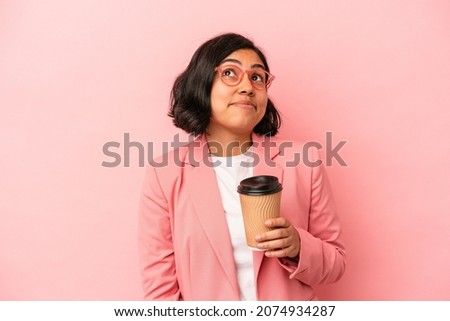 Young latin woman holding take away coffee isolated on pink background dreaming of achieving goals and purposes
