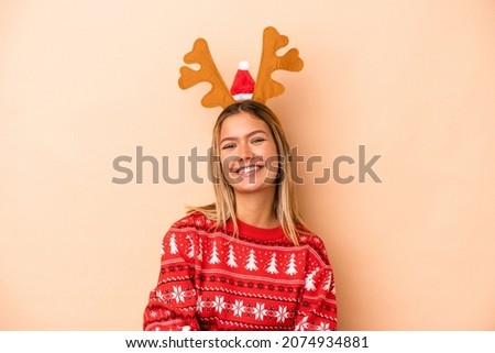 Young caucasian woman wearing a christmas reindeer hat isolated on beige background laughing and having fun.